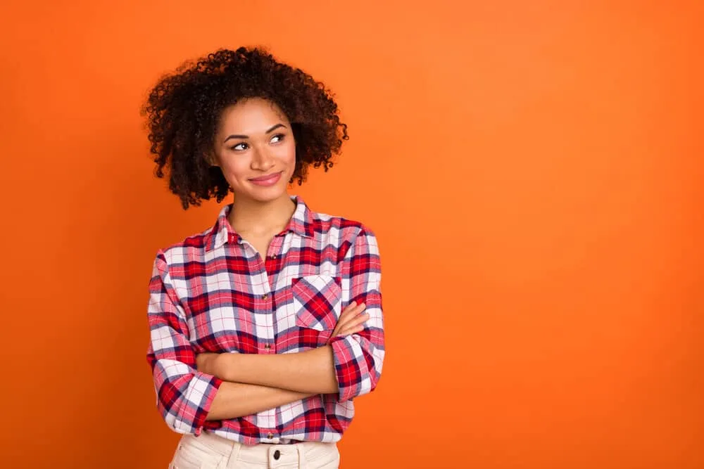 Why Is My Hair Getting Darker as I Get Older Instead of Gray 4 African American female with a dark brown eye color wearing a plaid shirt and beige jeans with kinky hair strands.