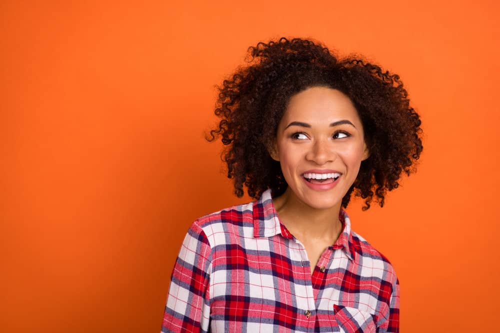 Young African American female showing off her hair after using the sun to naturally lighten her dark brown curls.