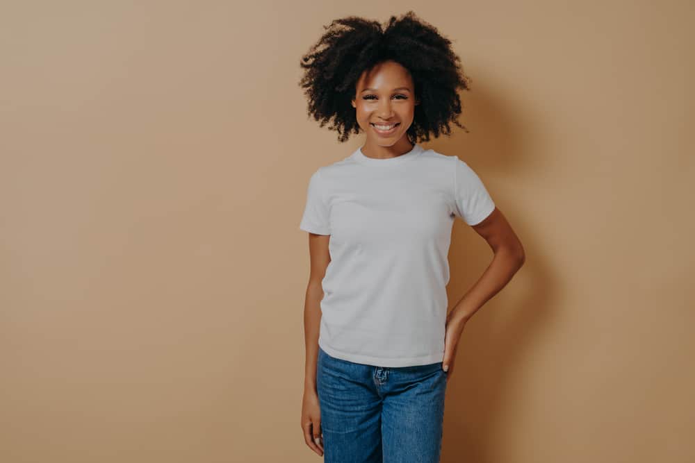 A dark-skinned black lady wearing a white t-shirt and jeans with 4A natural hair - curls and kinks.