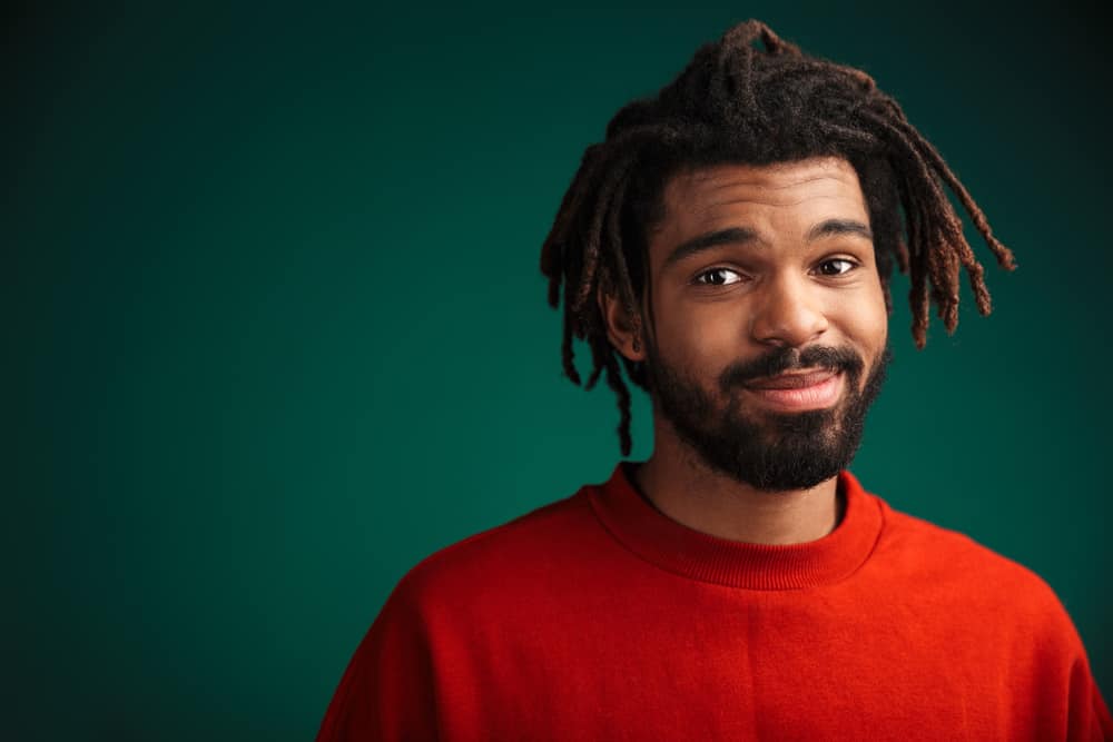 A black man wearing a red shirt after dyeing his dread tips while protecting it with a dark blue towel.