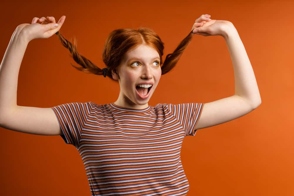 A lady having fun wearing pigtails on orange hair with war tones after using a blue toner.