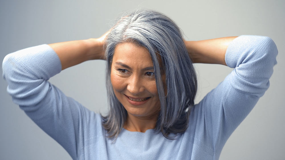 Cute Asian Woman with naturally gray hair and olive skin tone putting her darker hair in a ponytail. 