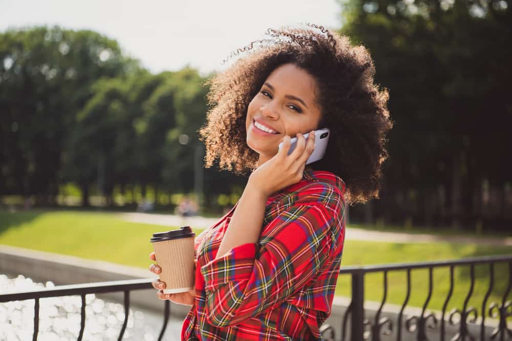 Young adult woman with a layered cut with longer layers than a traditional curly bob talking on the phone.