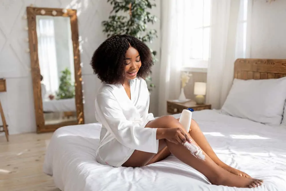 Dark-skinned African American female with body hair using a common hair removal method to shave legs.
