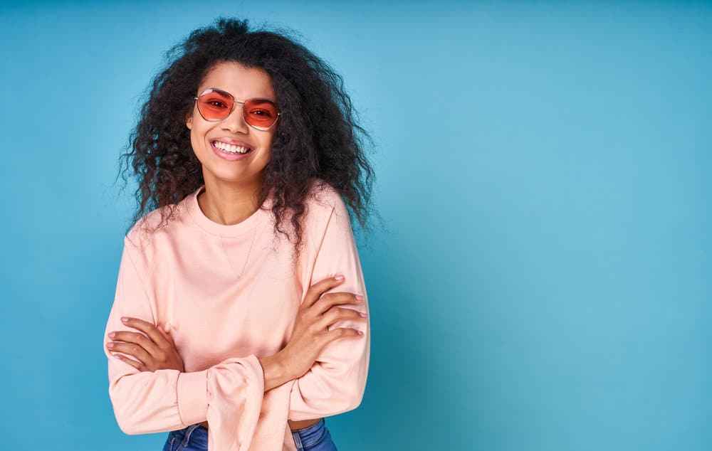 Joyful young African American female with frizzy hair has been following the Curly Girl Method on her natural waves.