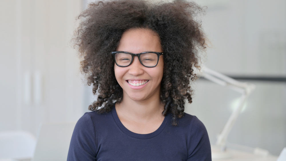 Young lady with a tapered wolf cut on thin hair with black eyeglasses and a blue t-shirt.