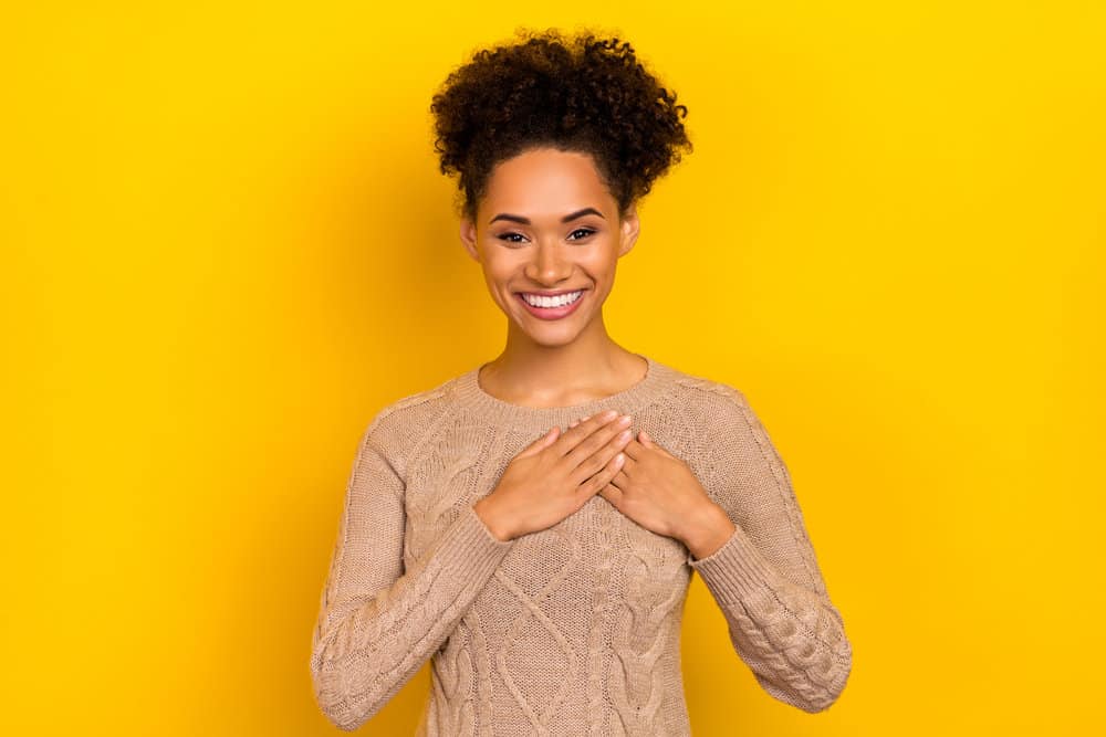 A black lady wearing a beige sweater with a curly hair texture has been eating a healthy diet to encourage hair growth.