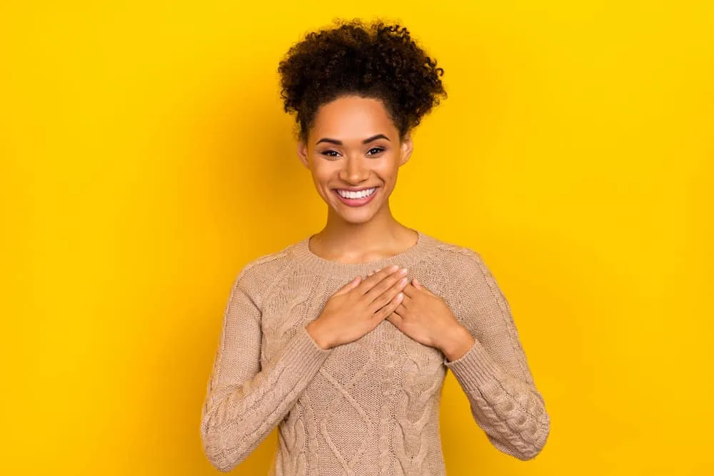 Why Does My Hair Grow Uneven? How to Fix Uneven Hair at Home 3 A black lady wearing a beige sweater with a curly hair texture has been eating a healthy diet to encourage hair growth.