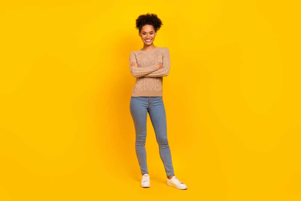Beautiful young African lady wearing a light brown sweater and stone-washed blue jeans with white sneakers.