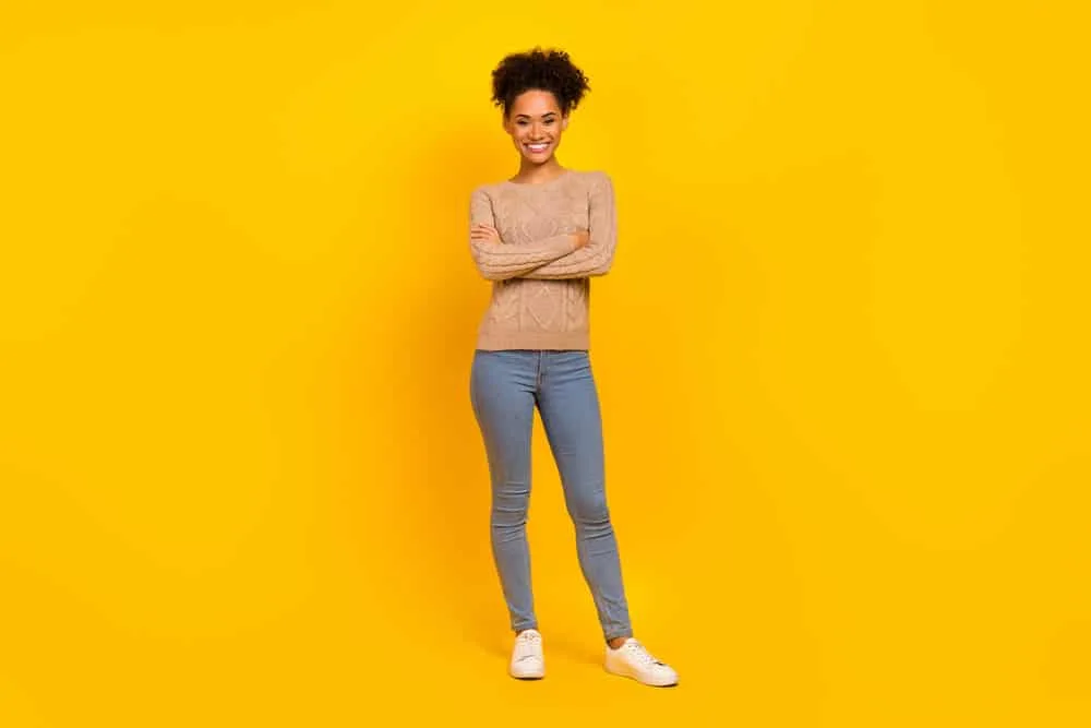 Why Does My Hair Grow Uneven? How to Fix Uneven Hair at Home 8 Beautiful young African lady wearing a light brown sweater and stone-washed blue jeans with white sneakers.