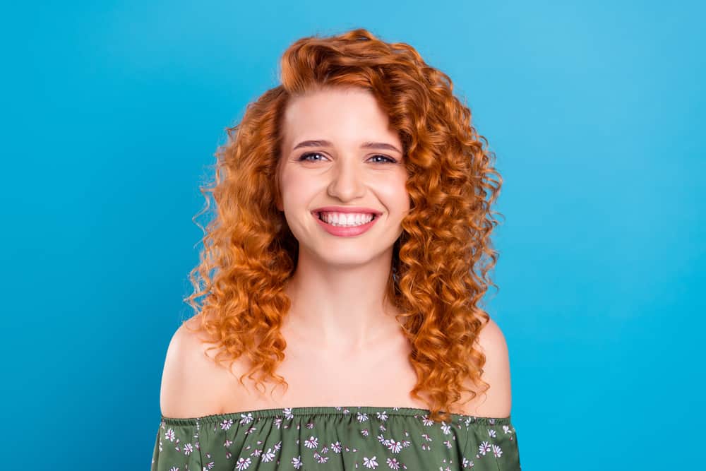 Cheerful young lady with ash-blonde dye covering her naturally red hair wearing a green shirt with flowers.