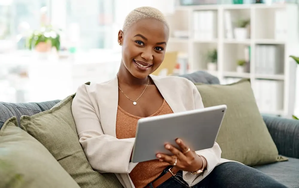 A black girl with finger coils styled with hair gel sitting on the couch reading her iPad.