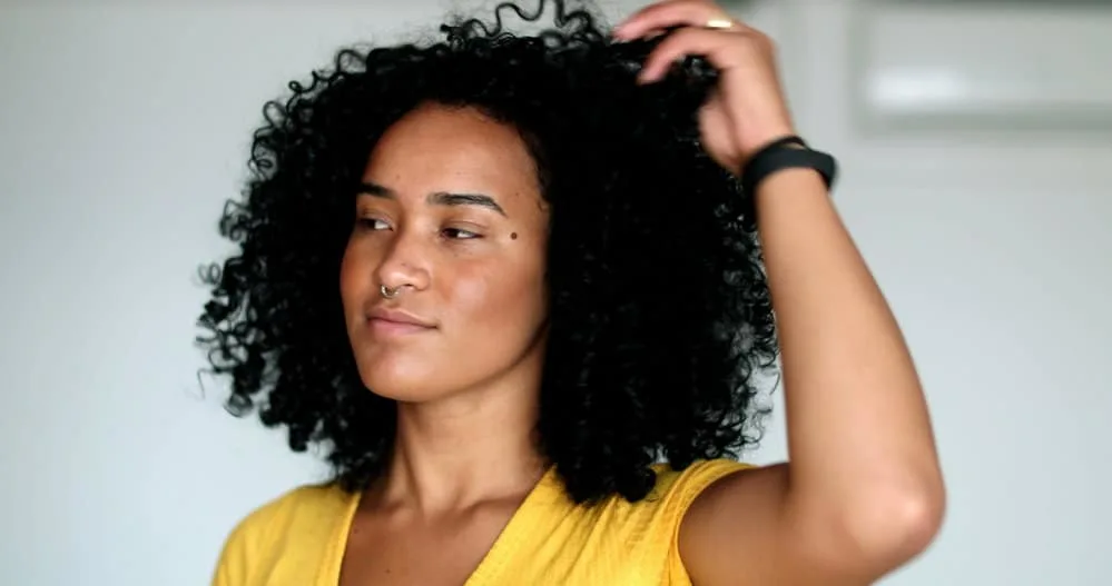 Young African American female with flat hair strands preparing to wear a silk bonnet before she goes to sleep at night.