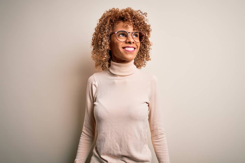African American female with curly hair, pink lipstick, colorful glasses, and a beige turtleneck sweater.