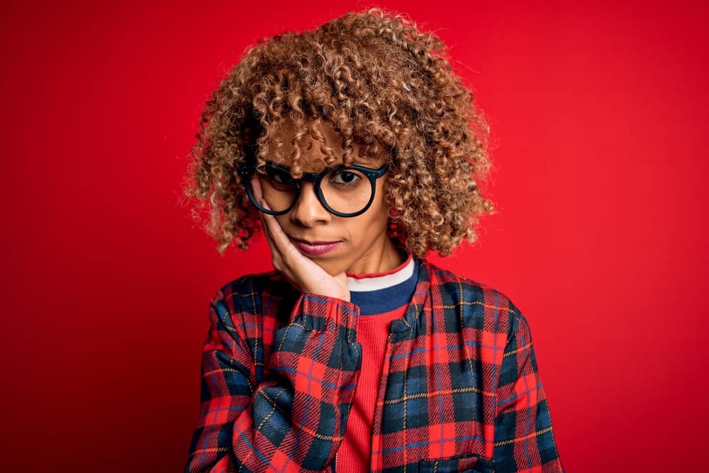 A frustrated black woman with porous hair after undergoing the hair bleaching process on her curly long hair.