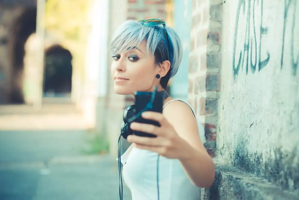 A fair-skinned, young woman with light brown hair taking a selfie after dyeing her hair blue.