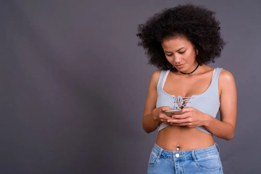 How Long Does It Take For Roots To Grow Out: Growing Out Natural Hair Color 8 A black girl with a belly ring using an iPhone to research the difference between baby shampoo and dry shampoo.