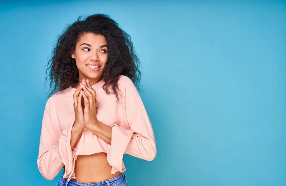 5 Best Products for Fine Wavy Hair: Shampoo, Oil, Gel, & More 14 A cheerful dark-skinned black lady with baby fine hair after styling her wavy strands with argan oil.