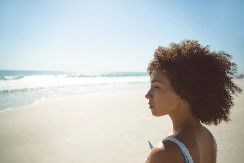 A light-skinned African American female with thick frizzy hair enjoying a very hot day at the beach in the sand.