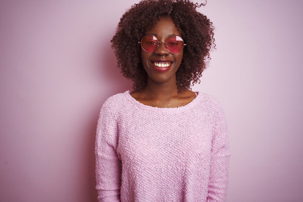 Young African American female covering her own hair with hair weft extensions to create a different hairstyle.