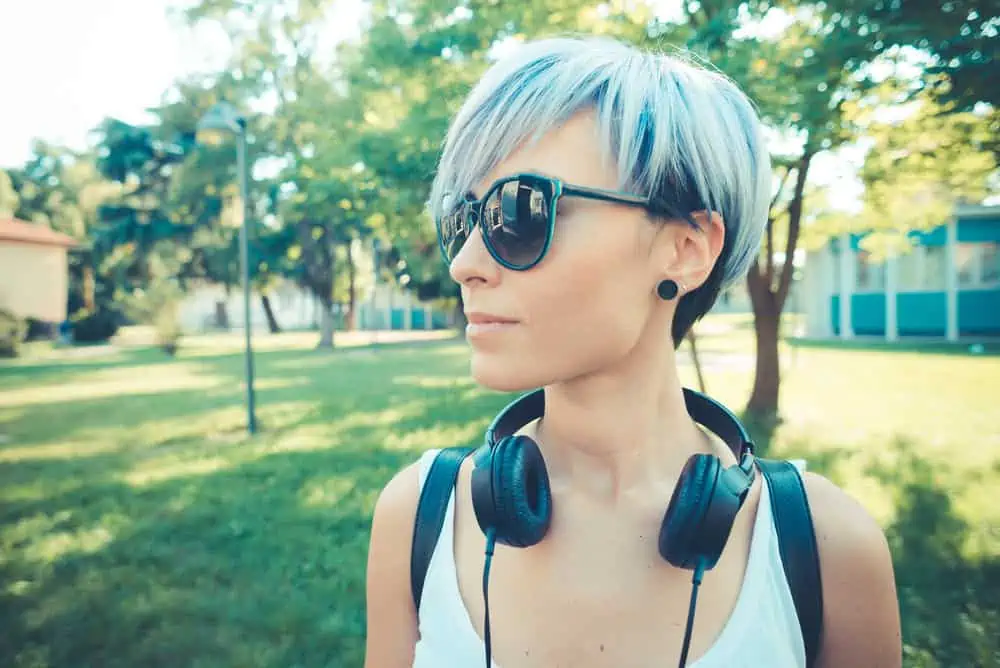 A young white woman wearing blue hair color with shades and headphones.