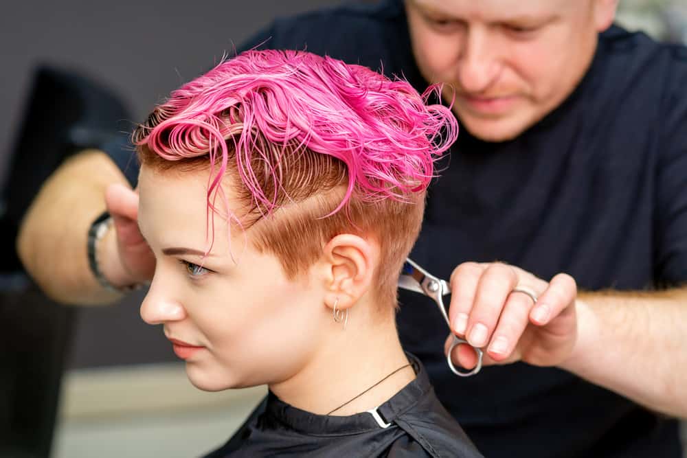 Lady with damaged hair and a pink hand-painted color on straight hair strands asking about salon prices.