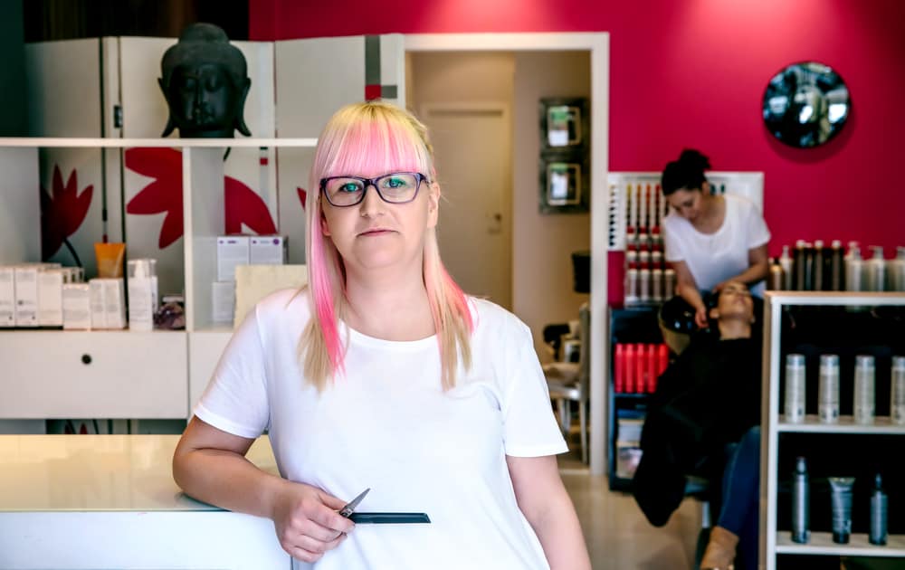 A lady hairdresser in a hair and beauty salon washing a customer's hair in the background.