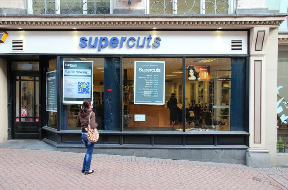 A woman outside of an individual business location of Supercuts reviewing salon services and current pricing.