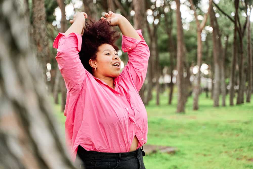 A chocolate brown-skinned female with shoulder-length curls with unwanted tones pulling her own hair upward.