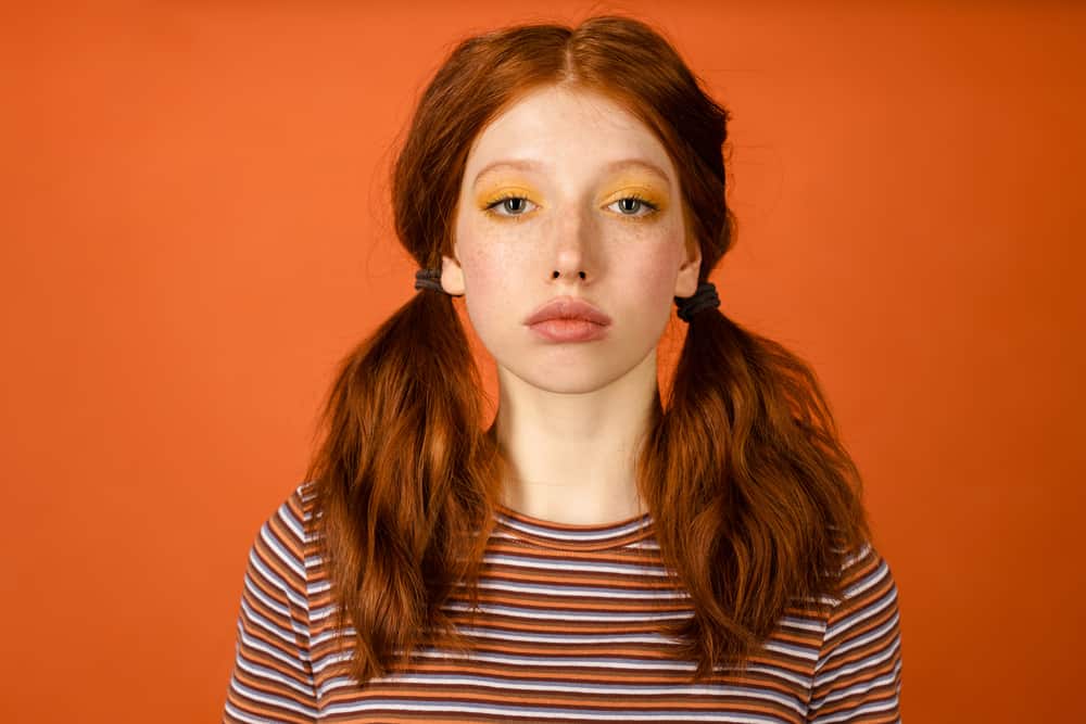 Young women with brassy orange natural hair color wearing bright orange eye shadow and striped shirt.