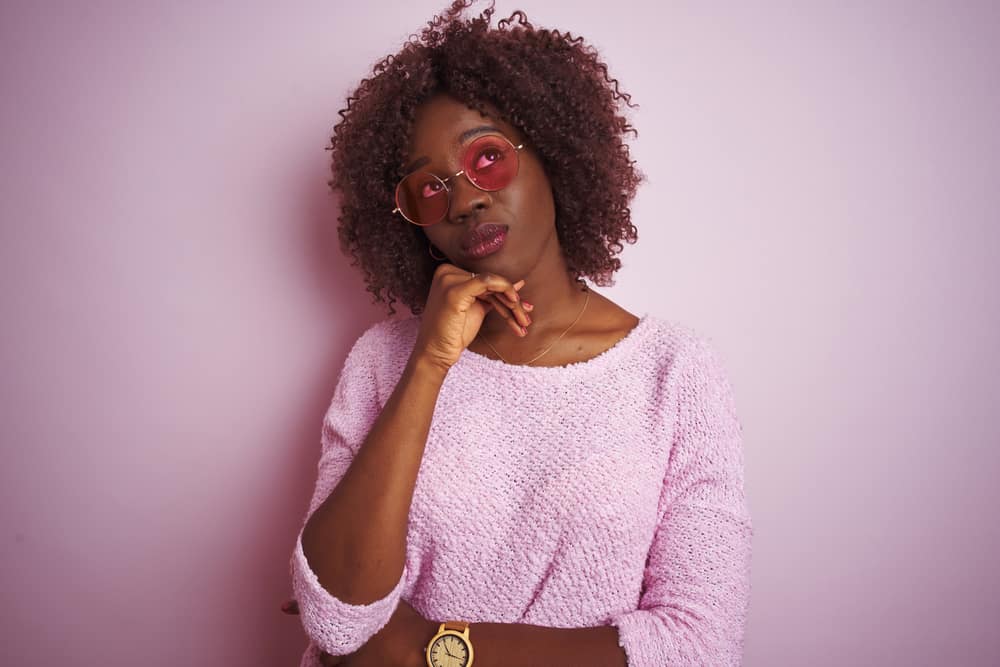 Thoughtful young black girl wearing dark brown hair color to cover up damaged strands from heat styling.