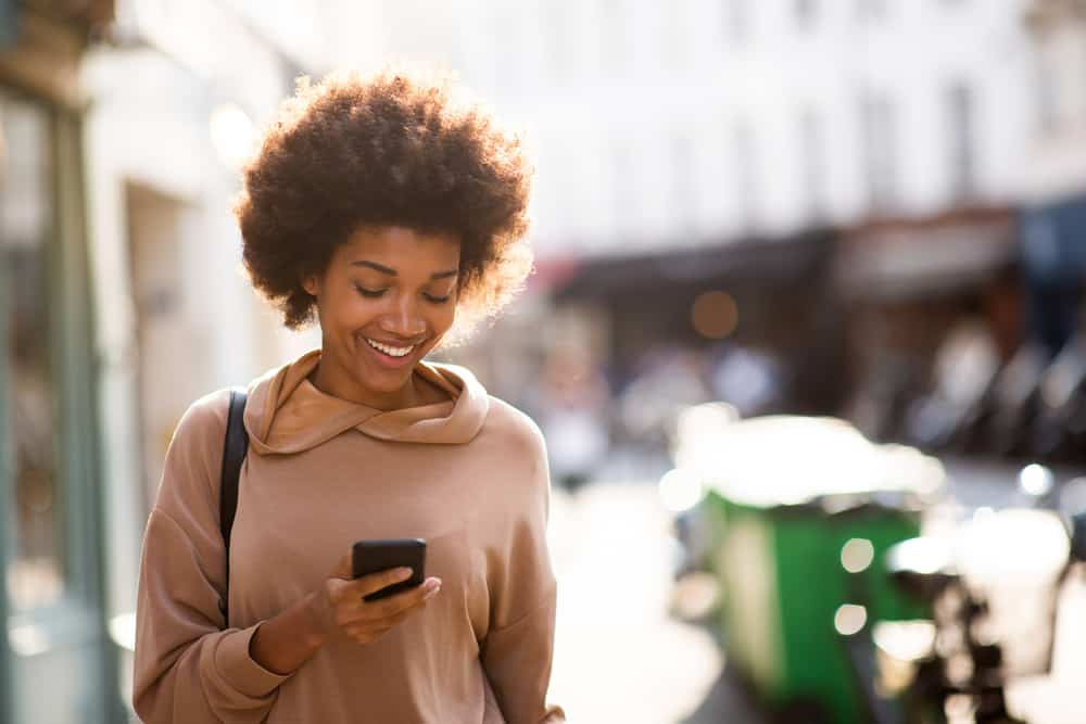 Young black woman wearing kinky hair extensions on her curly long hair strands while walking down the street.