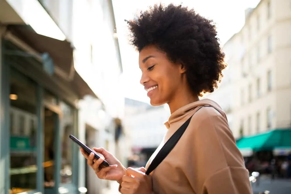 Why Is My Hair Matting Underneath? Prevent Hair From Matting 3 African American female with acute hair matting researching how to detangle matted hair on her mobile phone.