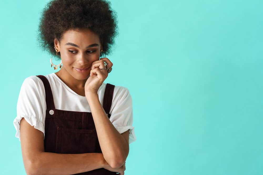 A black woman with a subtle smile and dark brown curls after going through the hair dyeing process.