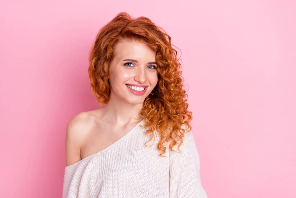 White girl with loose curls on a dark red hair color styled with ethnic products wearing a white sweater.