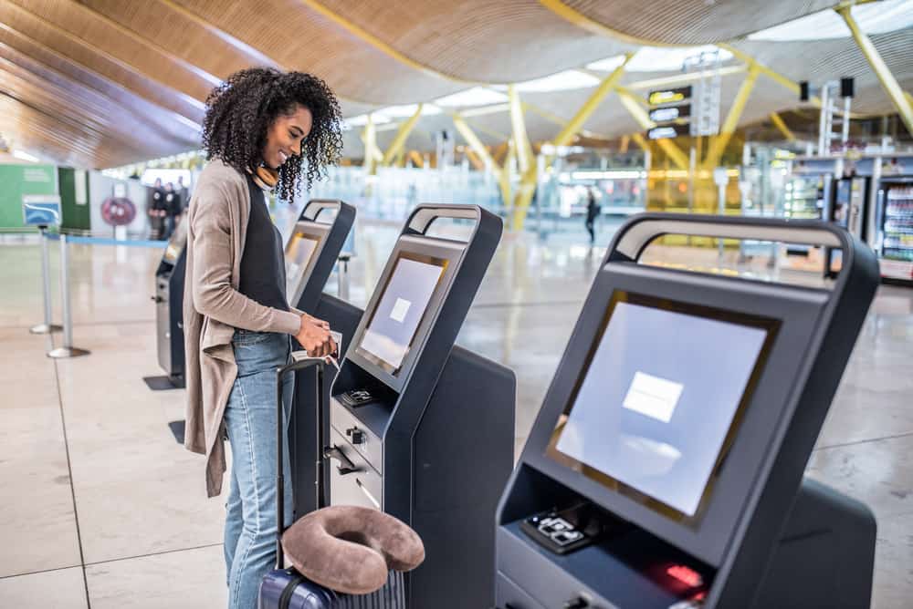 Black woman with curly hair getting a boarding pass while researching if hair spray will be ok in her checked baggage.