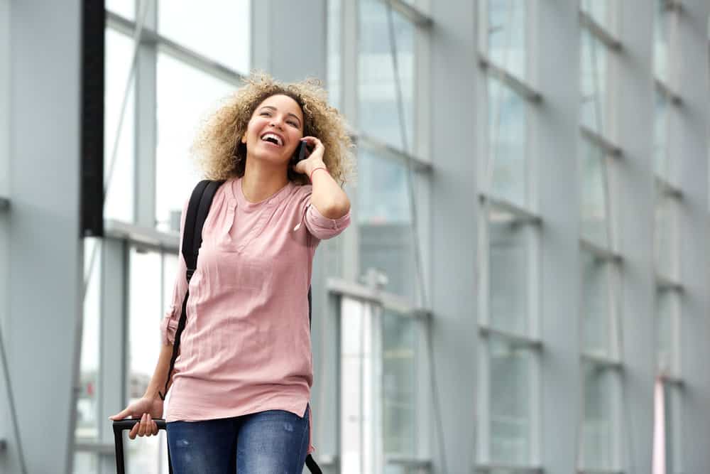 Young traveler talking on the phone while carrying electric clippers in her hand luggage before boarding an airplane.