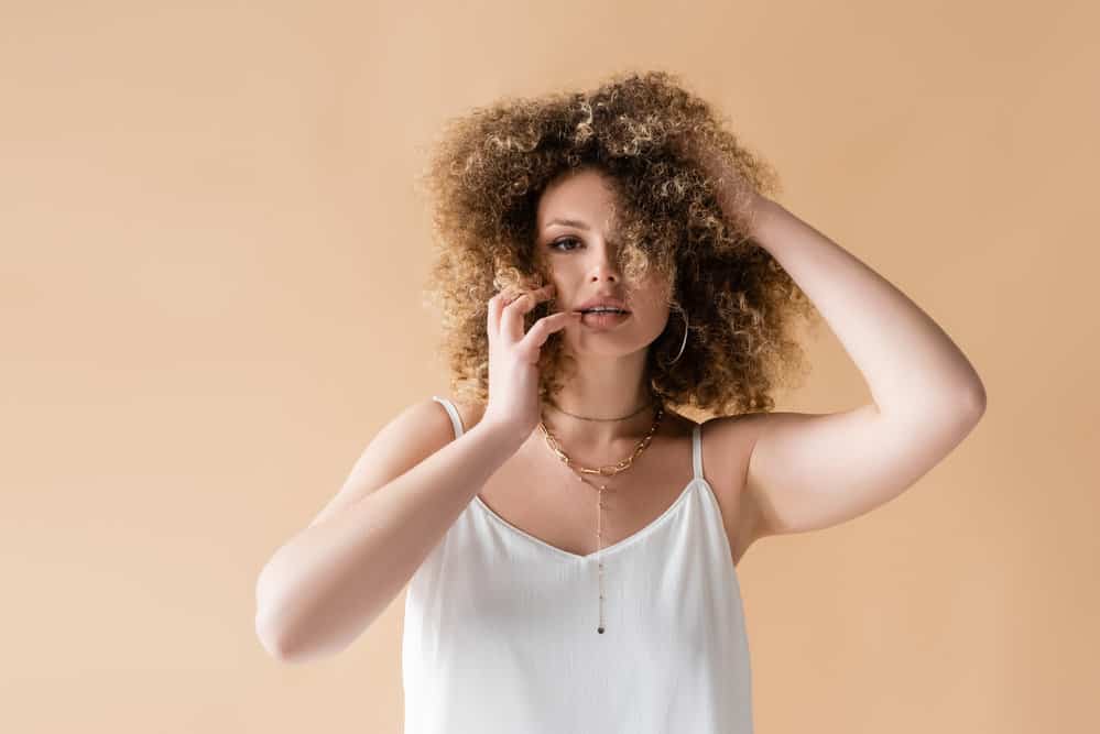 A young white woman with green eyes wearing a curly hairdo styled with jojoba oil and Shea Moisture hair products.