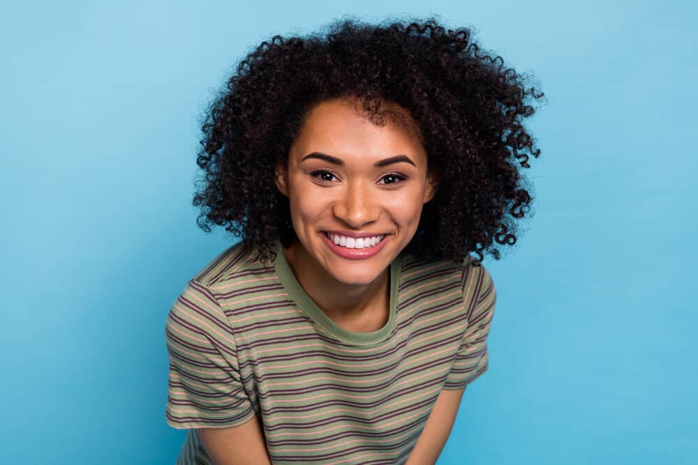 Light skinned black female with flawless skin after using a moisturizing hair mask on her dark brown dry hair strands.