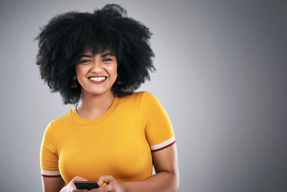 African American lady with natural curls styled with coconut oil wearing a t-shirt that's a gold color.