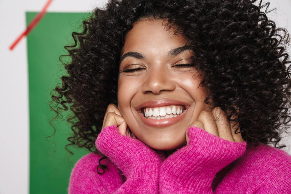 A black woman with curly hair follicles dealing with scalp psoriasis leads to an itchy scalp and mild dandruff.