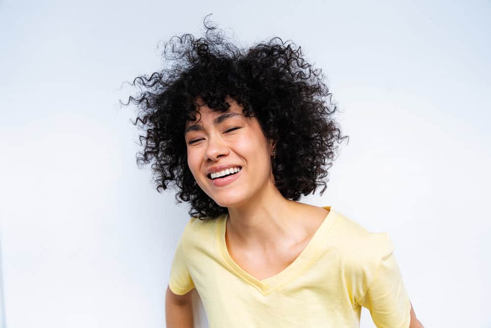 Young lady with perfect skin and bouncy curls after using skin toner and styling her hair with rice water ice cubes.