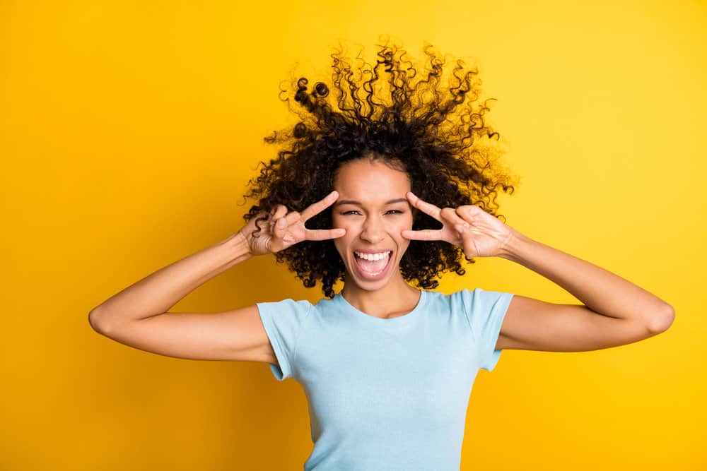 A cute young black lady wearing a light blue shirt with naturally black curly hair styled with semi-permanent dyes.