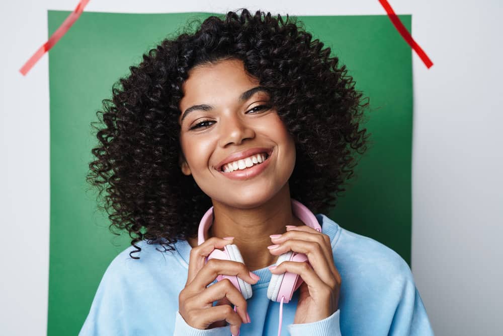 A joyful African American woman with an itchy scalp and white flakes on curly thick hair suffering from hair fall.