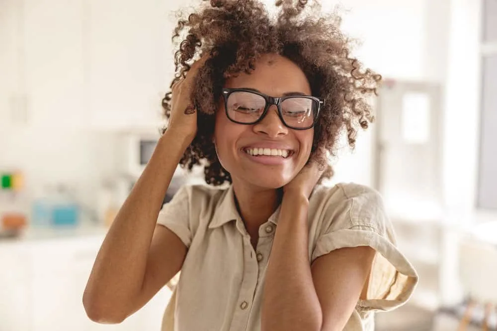 Does Olaplex Shampoo Make Your Hair Greasy or Oily? 3 African American female with towel-dried hair enjoying her natural curls after using Olaplex shampoo and conditioner.