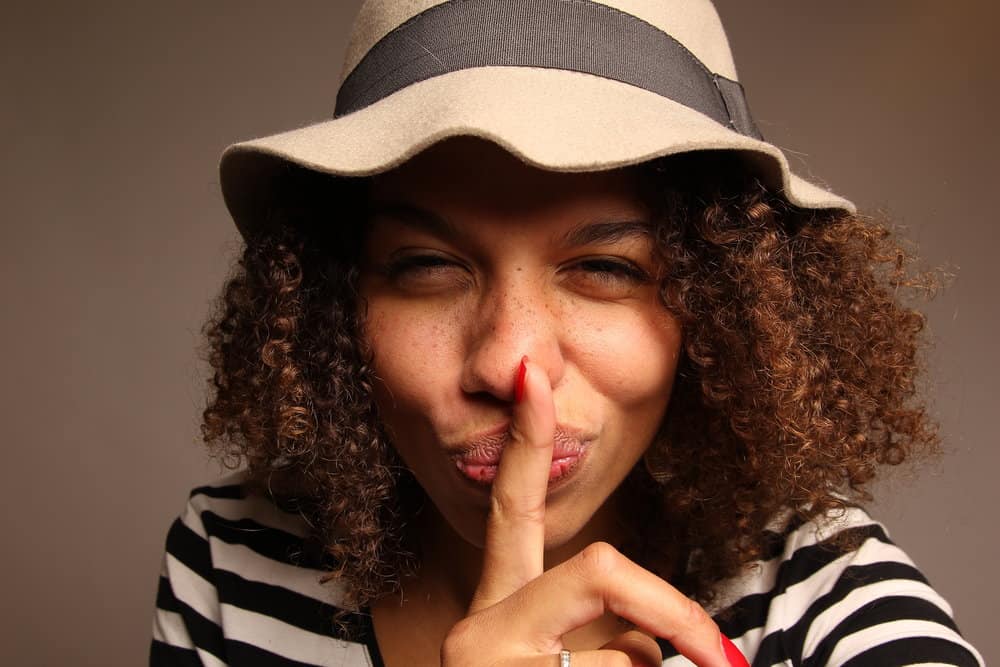 African American woman wearing her hair red in a very curly style wearing a cap to protect her curls from the sun.