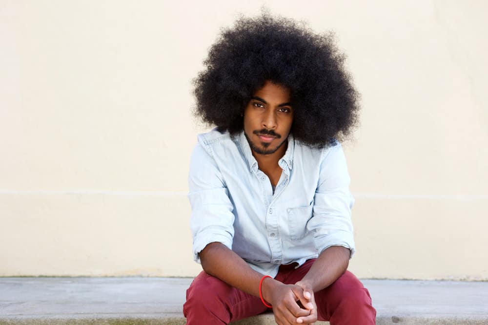 A serious young man that has patiently seen his hair grow into long locks after avoiding the barber shop.