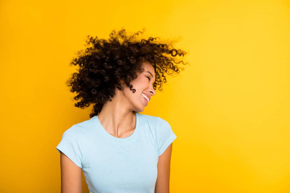 A charming lady wearing temporary hair dye on her 3A natural curls and a light blue shirt while dancing outside.