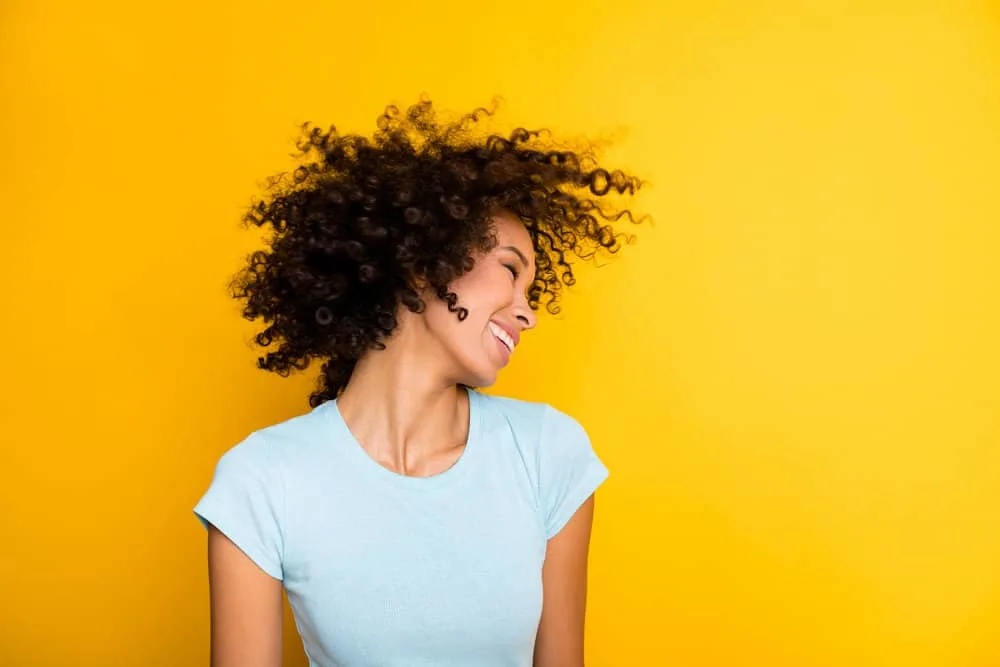 Can You Bleach Over Semi-Permanent Hair Dye? What Happens? 4 A charming lady wearing temporary hair dye on her 3A natural curls and a light blue shirt while dancing outside.