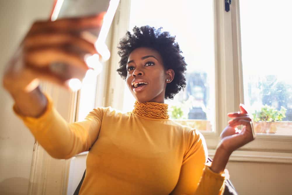 Cute African American female with long hair using a hairstyle try-on app to find the best hairstyles for her face shape.